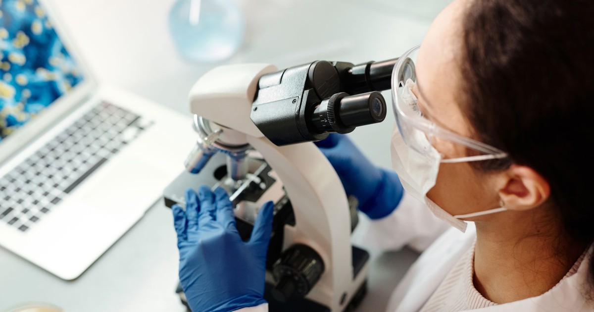 Scientist in protective gear examining samples with microscope in laboratory setting.