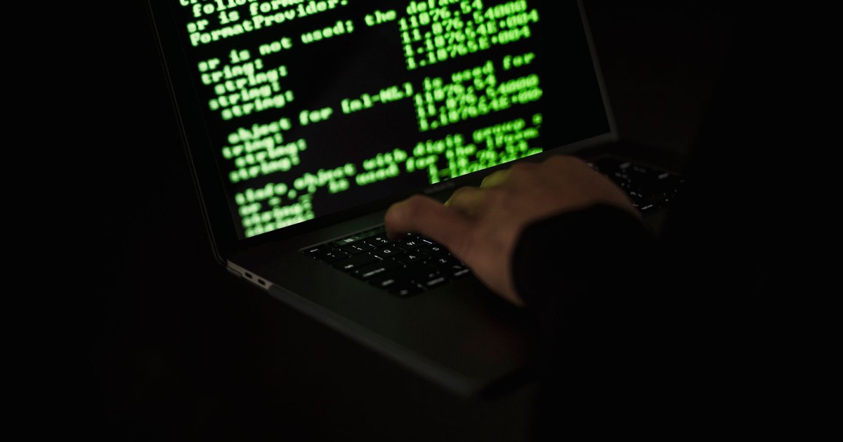 Crop unrecognizable computer geek typing on netbook with codes on screen while hacking system in darkness