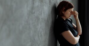 New Review Finds Strong Link Between Cannabis Use Disorder and Major Depression A woman in stress with eyes closed, leaning against a concrete wall indoors.