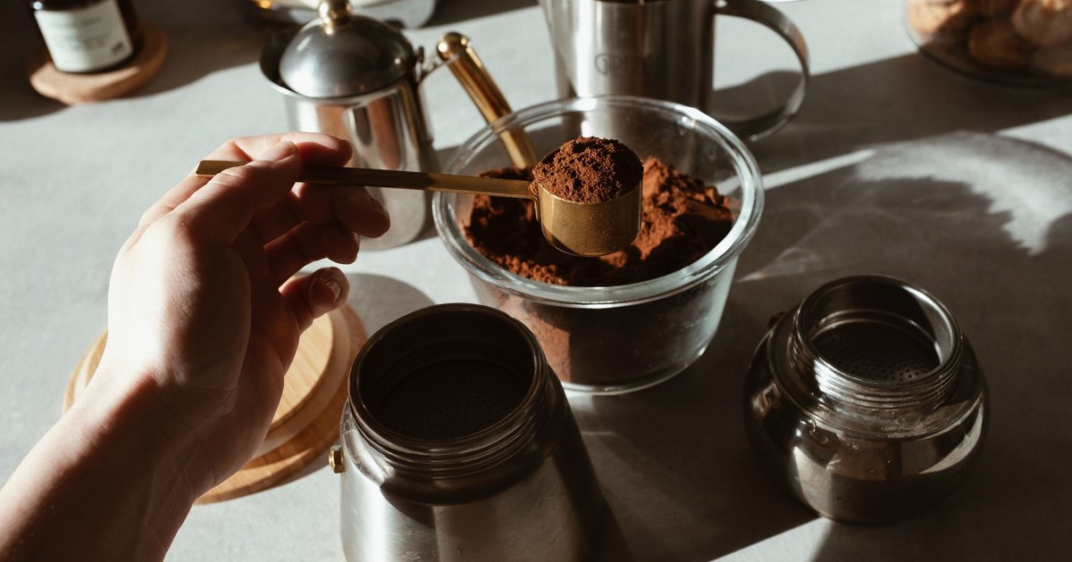 Hand scooping ground coffee from jar with kitchenware setup, ideal for morning brews.