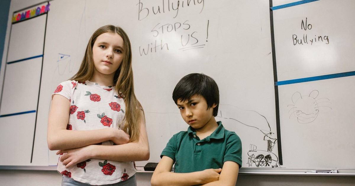 Children posing with 'Bullying Stops with Us!' message on classroom whiteboard.