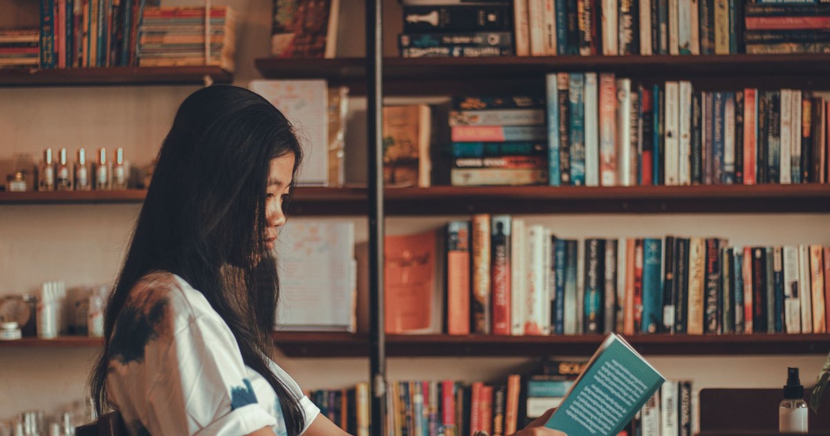 A young woman reads a book in a comfortable library with shelves full of books, offering a serene setting for relaxation.