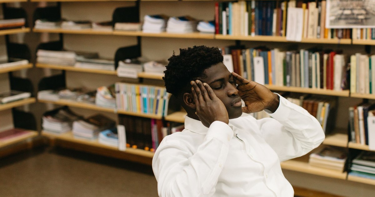 A man sitting in a library with hands on head, reflecting and relaxing.