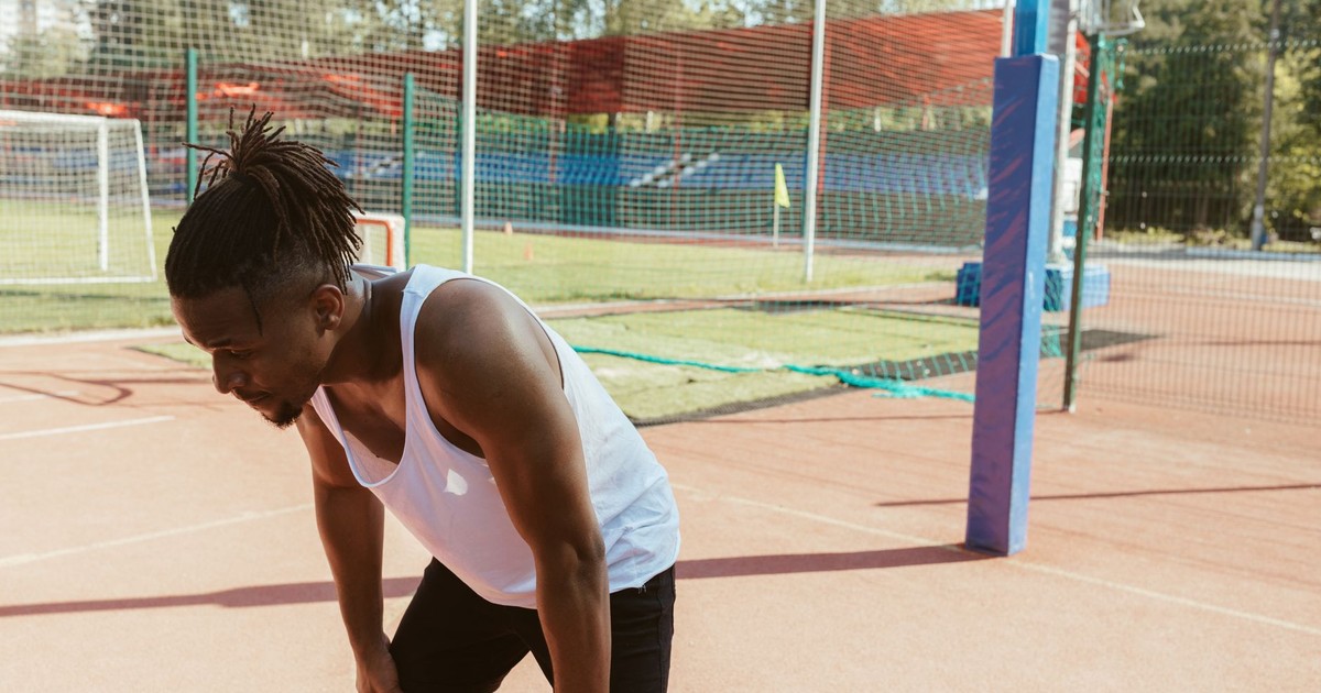 Tired athlete resting after exercise on a sunny outdoor sports field.