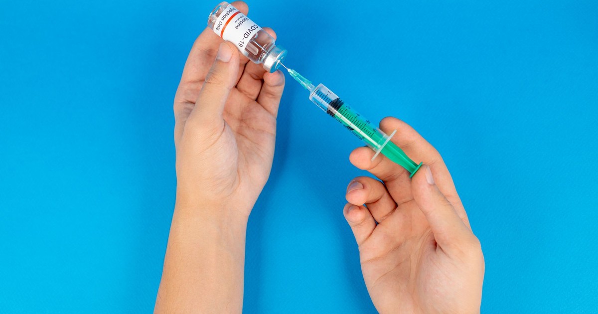 Hands holding a syringe and COVID-19 vaccine vial on a blue background.