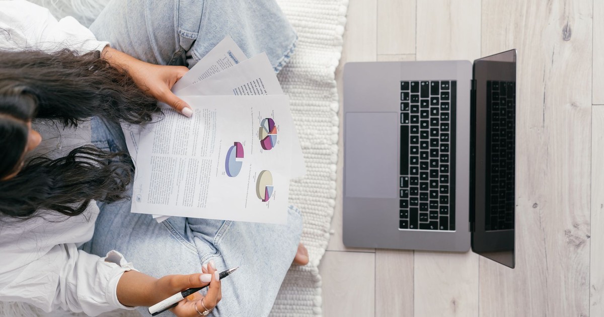 Top view of a woman studying charts on paper with a laptop, focusing on education and technology.