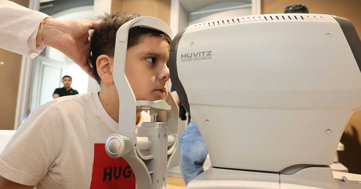 Young boy receiving an eye exam using autorefractor at a clinic. Healthcare concept.