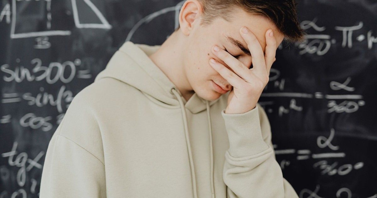 Young man overwhelmed by mathematical calculations on a blackboard in a classroom setting.