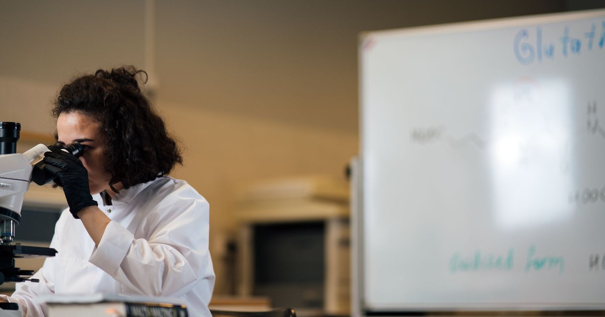 Female scientist examining samples under a microscope in a laboratory setting.