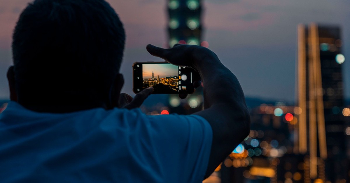 A man capturing a city skyline with his smartphone during dusk, highlighting urban photography.