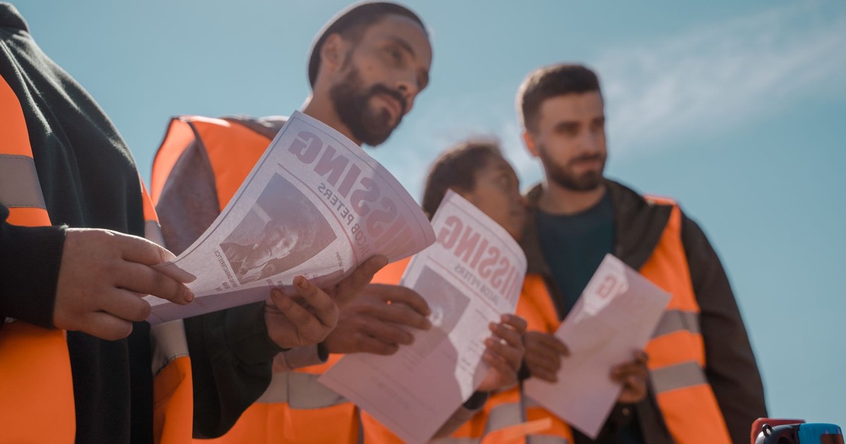 Group of volunteers in orange vests distributing missing person flyers outdoors.