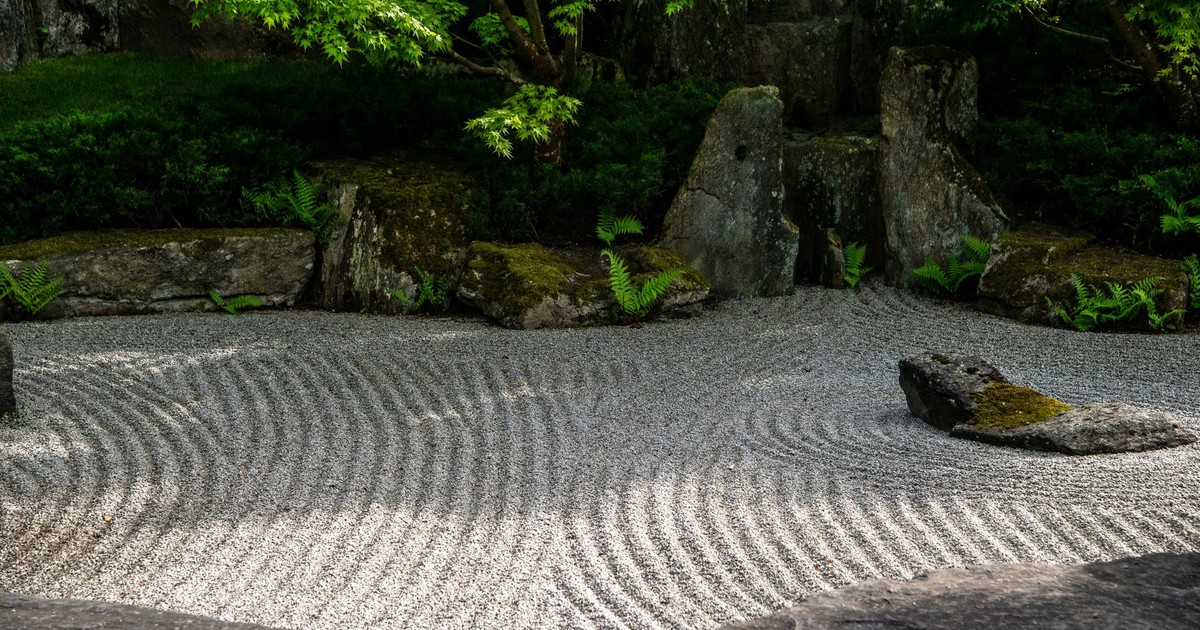 Peaceful Japanese Zen garden featuring meticulously raked sand patterns and lush green foliage.