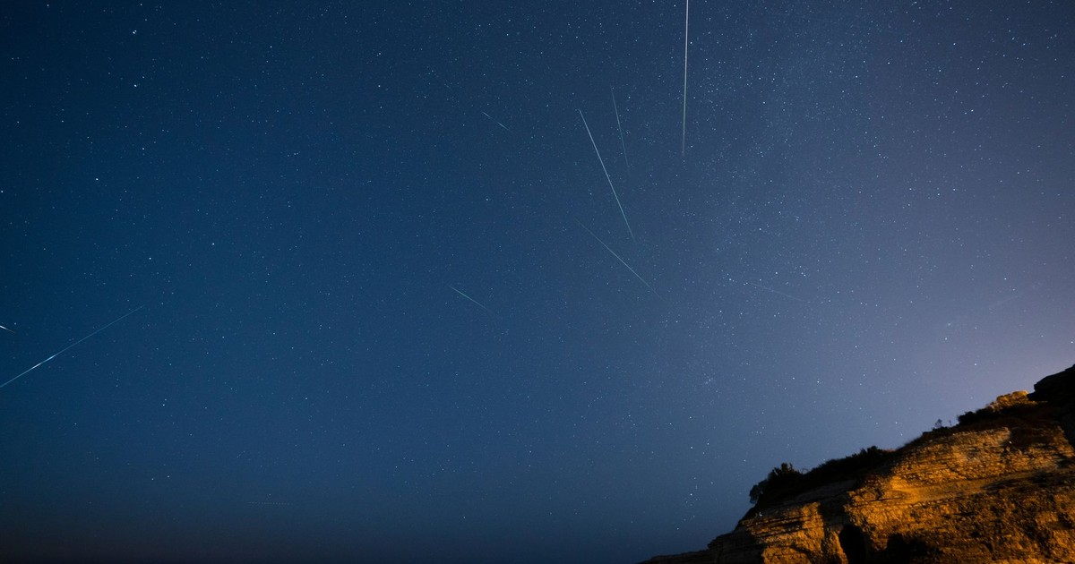 Beautiful starry sky with meteors streaking over a rocky cliff at night.