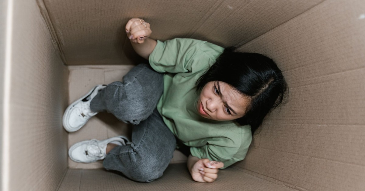 A woman feeling trapped and anxious inside a small cardboard box, symbolizing claustrophobia.