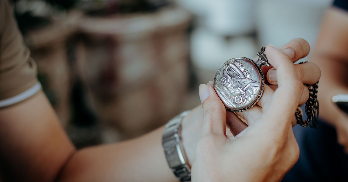 Detailed view of hands holding an antique pocket watch with chain outdoors.
