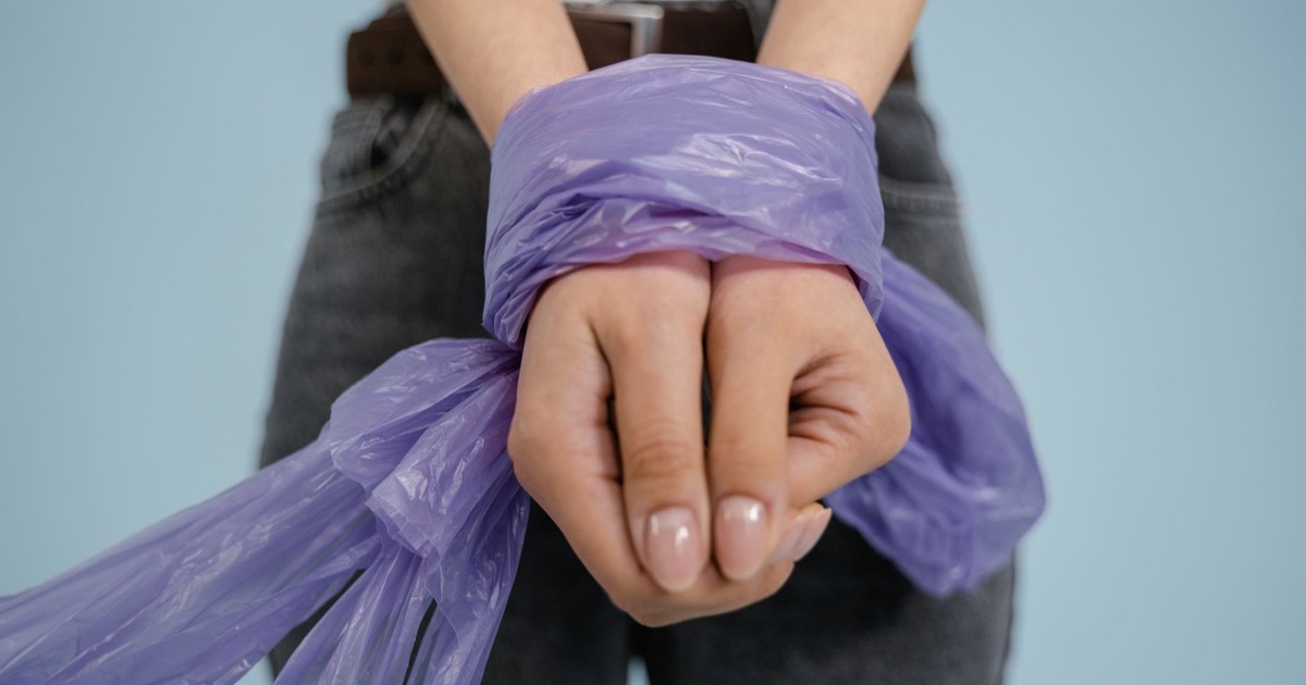 A close-up shot of hands tied with purple plastic against a light blue background.
