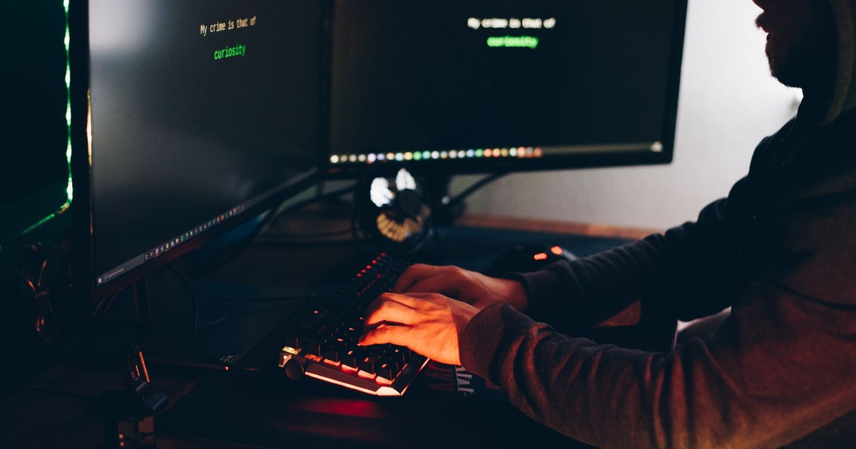 Side view of crop anonymous male cyber thief accessing information on desktop computer screens at dusk