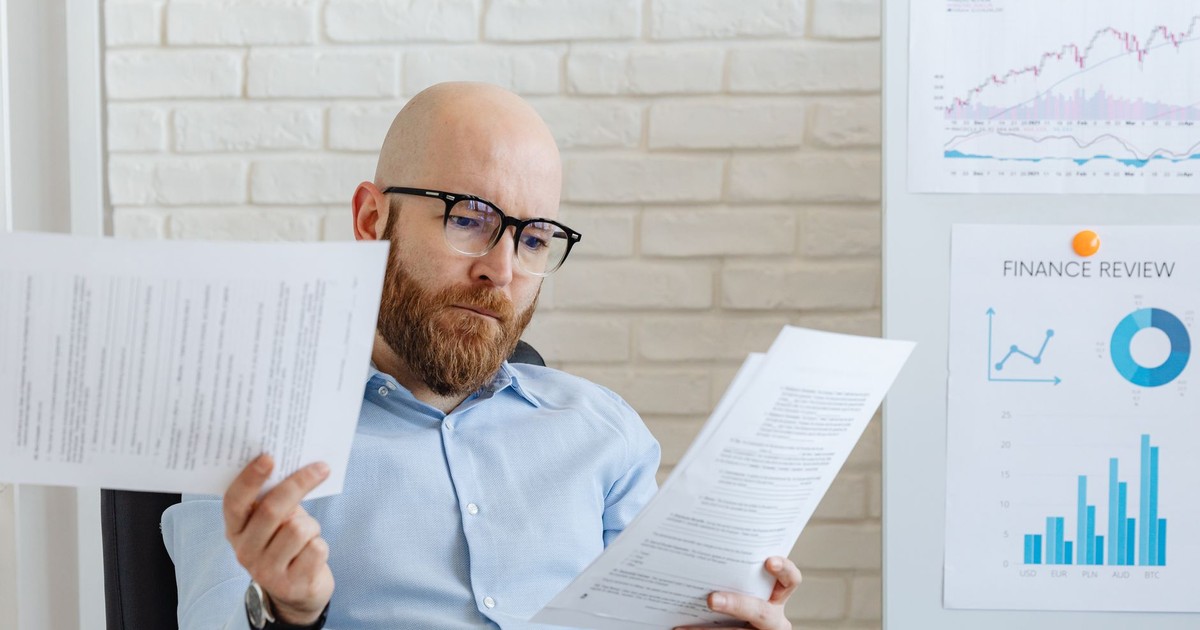 Bald bearded businessman reading financial documents in modern office setting.
