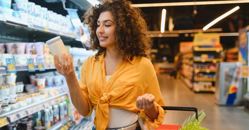 Young woman shopping for groceries, prioritizing healthy food choices by carefully reading the yogurt label in the dairy aisle