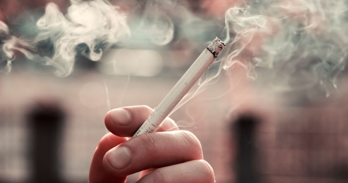 A close-up view of a hand holding a lit cigarette, with smoke visible in the air.