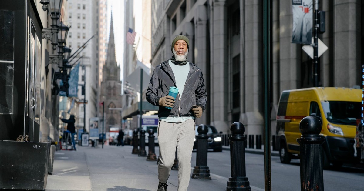 Senior man wearing activewear carrying a water bottle while walking in a bustling city street.