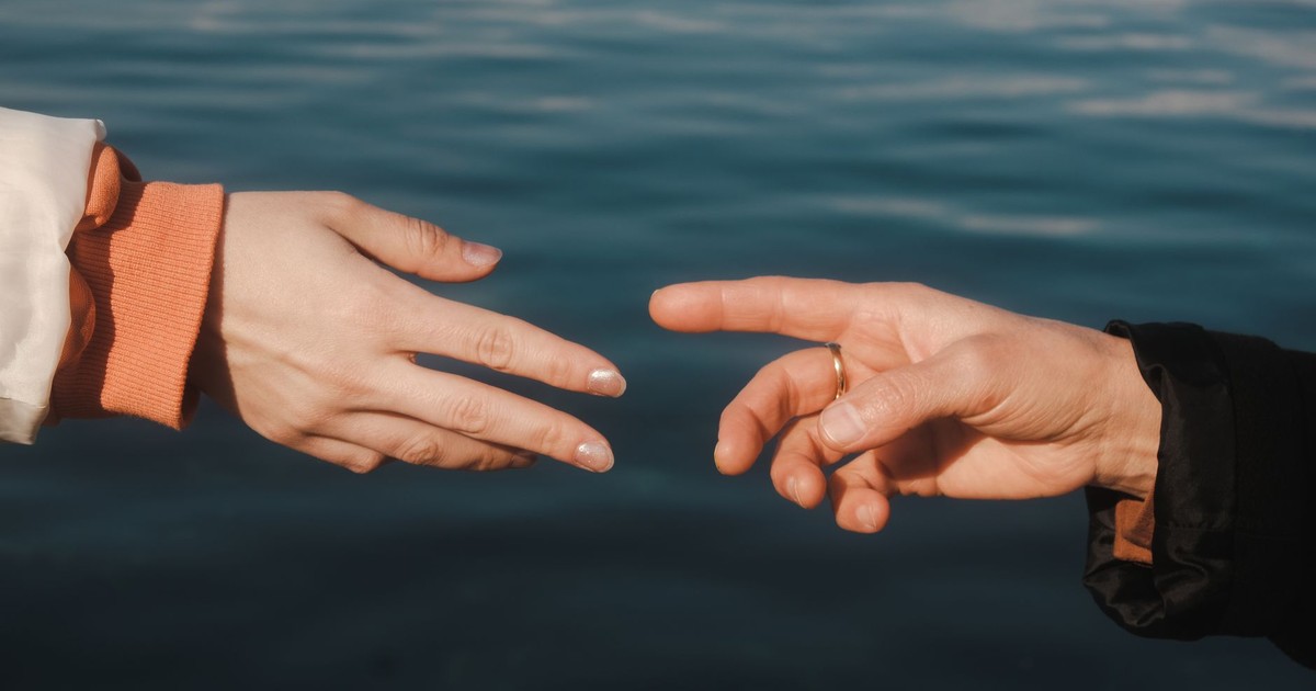 Two hands reaching towards each other over a tranquil blue sea background, creating a sense of connection.