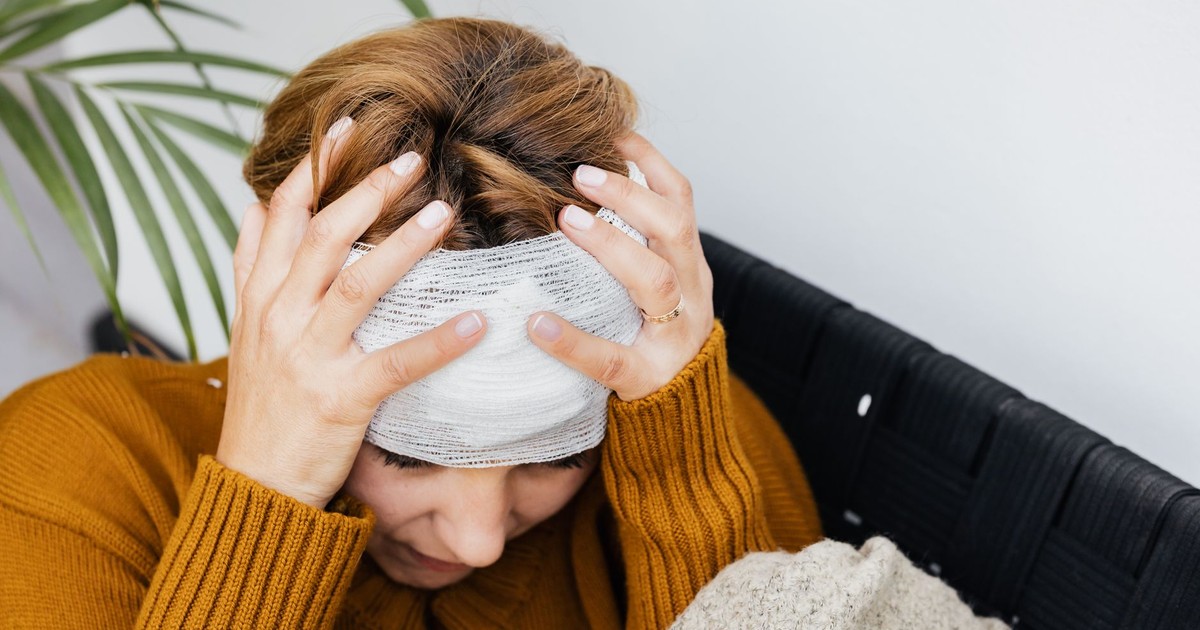 Woman with head injury holding her head in pain indoors.