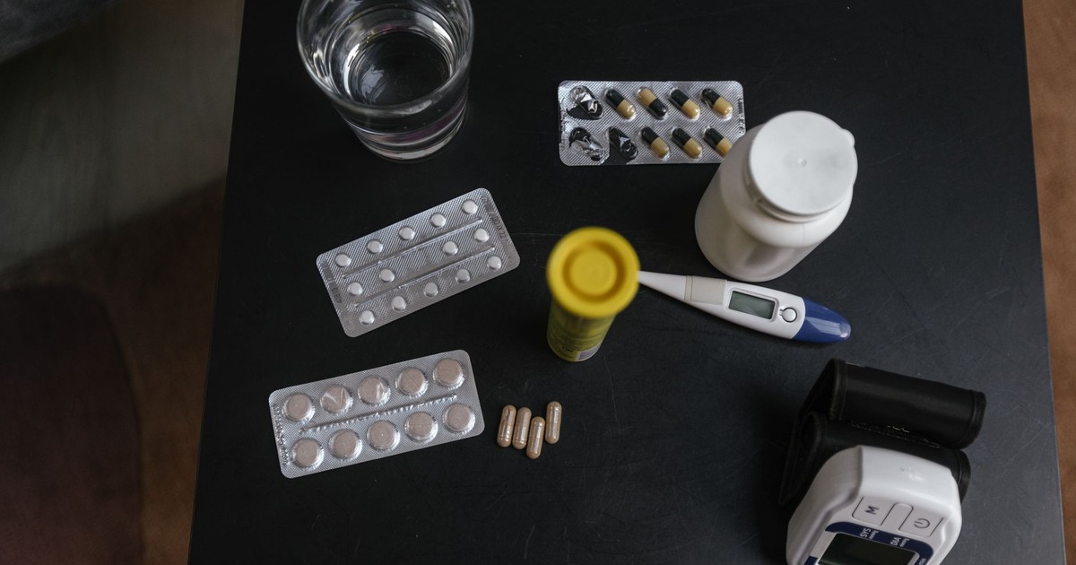 Top view of various medications, tablets, and medical devices on a table with a glass of water.