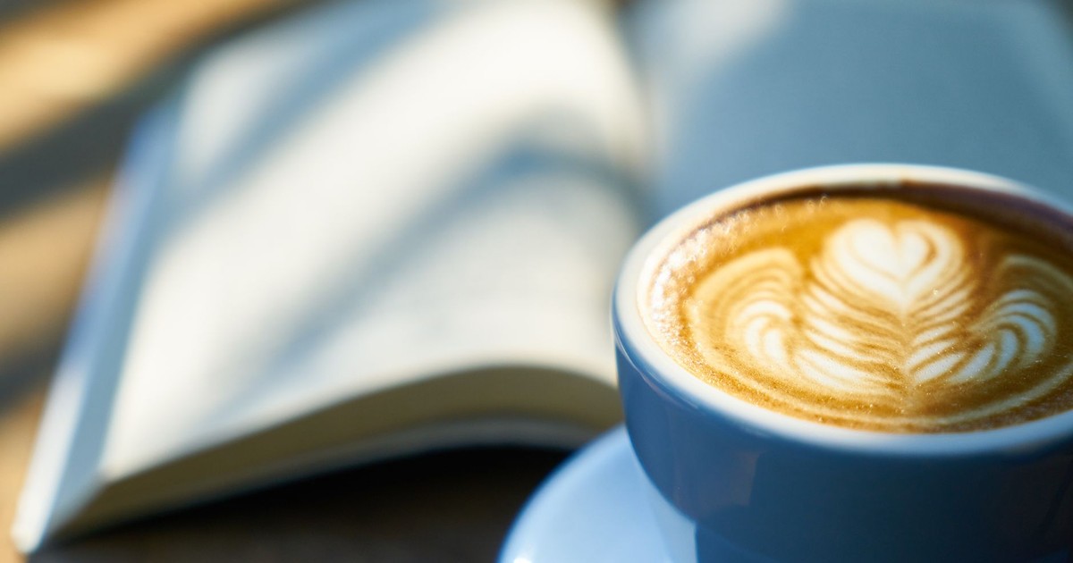 Warm latte art in a blue cup beside an open book, capturing a cozy morning vibe.