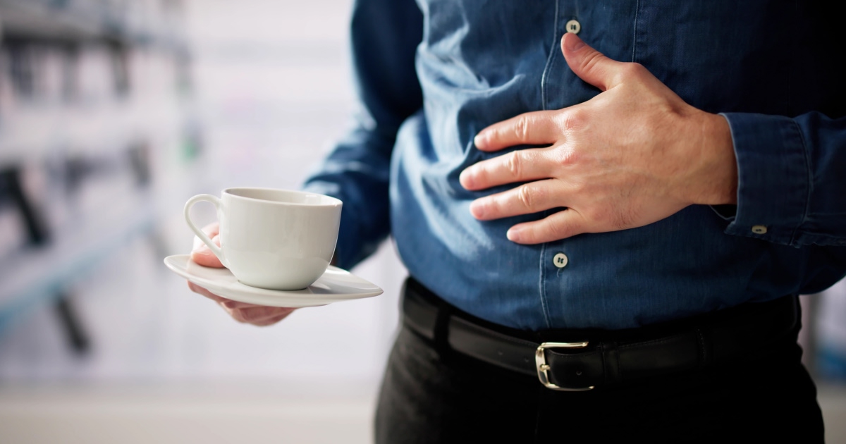 man holding hand over abdomen while holding cup of coffee