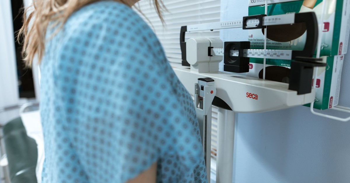 Adult female using a medical weighing scale in a healthcare setting.