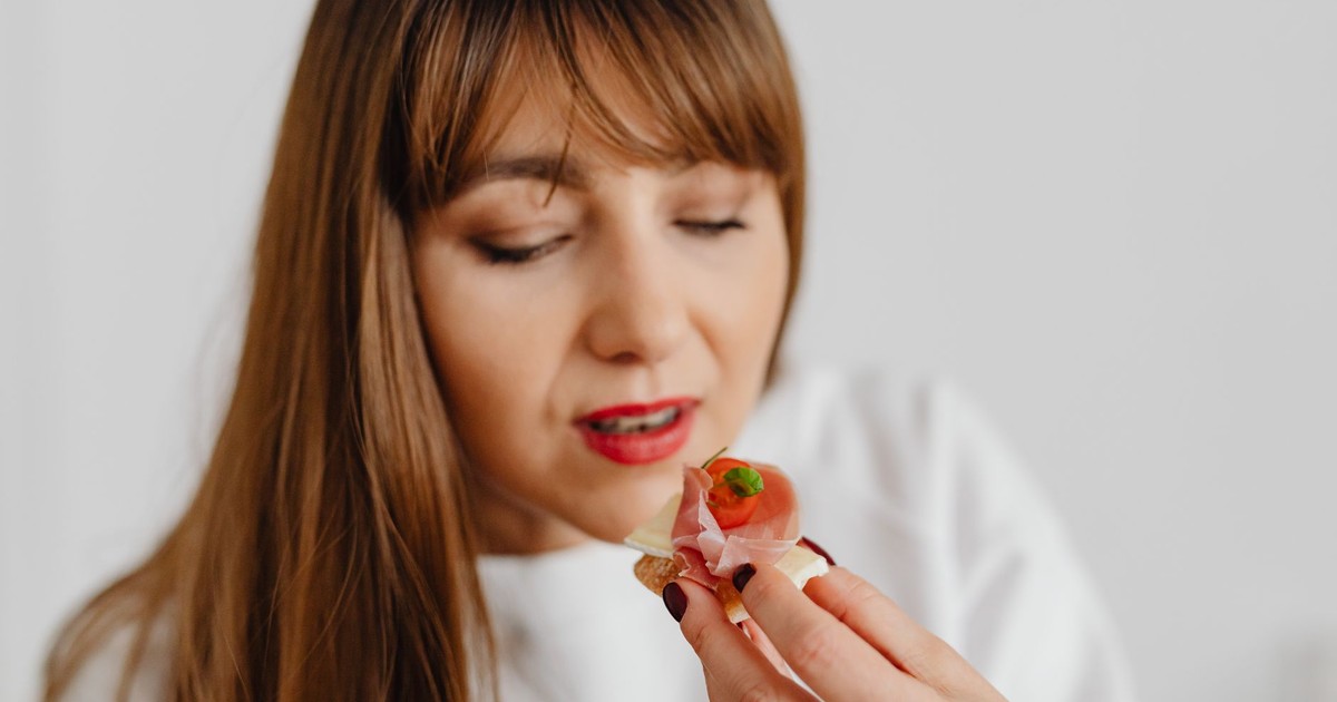Woman with long hair savoring a gourmet canape indoors.