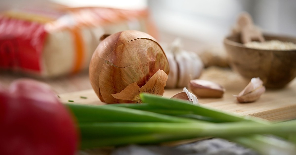Close-up of fresh onions, garlic, and peppers on a rustic kitchen table, perfect for culinary themes.